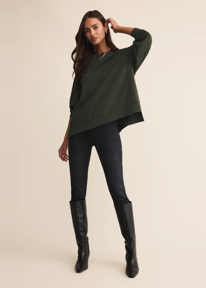 Woman wearing a dark green sweatshirt with black pants standing in front of a white background