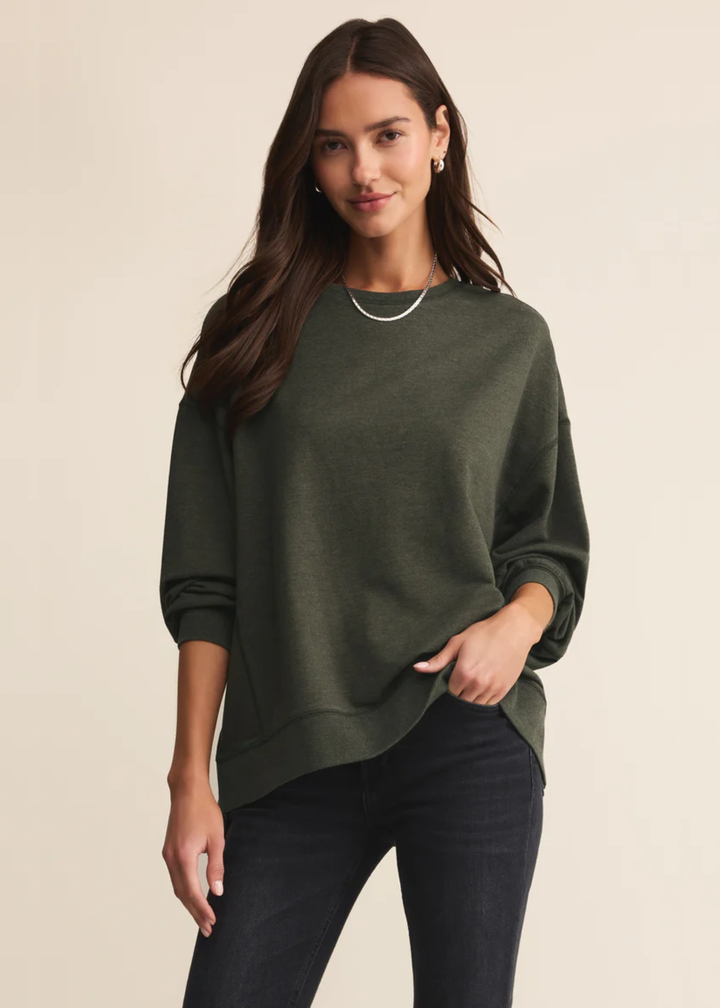 Woman wearing a dark green sweatshirt with black pants standing in front of a white background