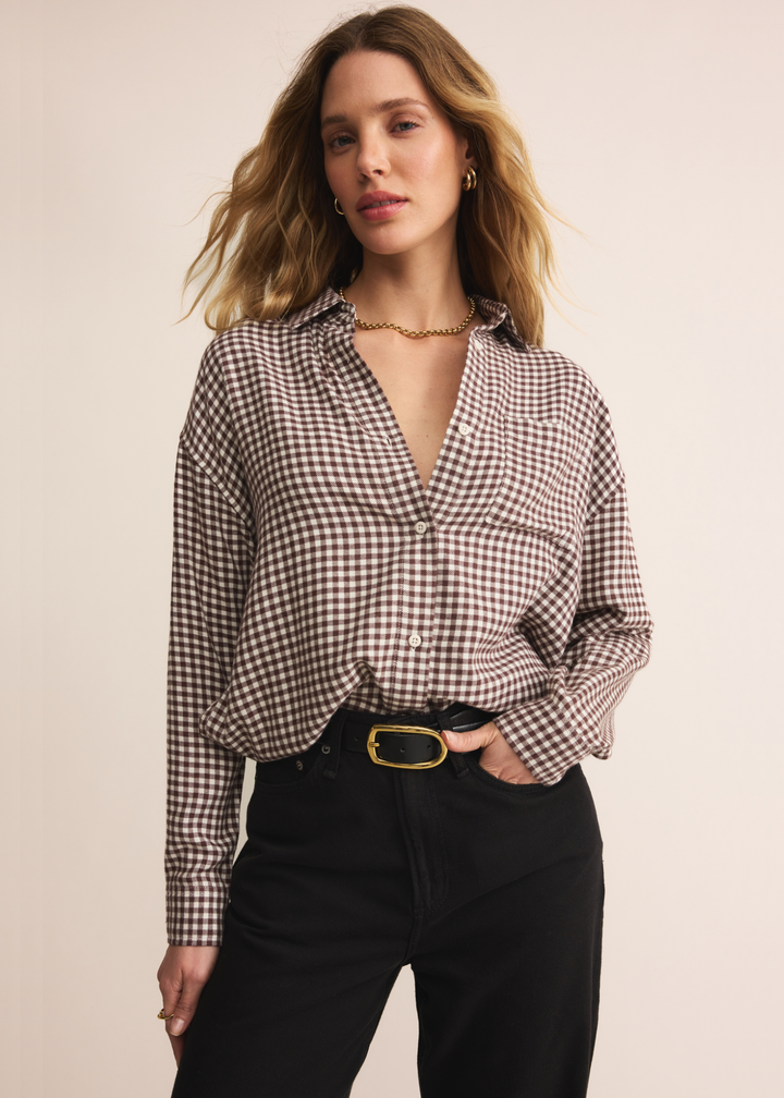Woman wearing a brown and white plaid button up with dark jeans standing in front of a white background