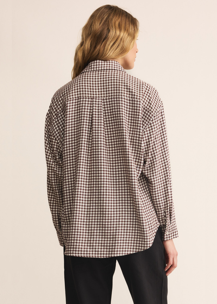 Woman turned around wearing a brown and white plaid button up with dark jeans standing in front of a white background