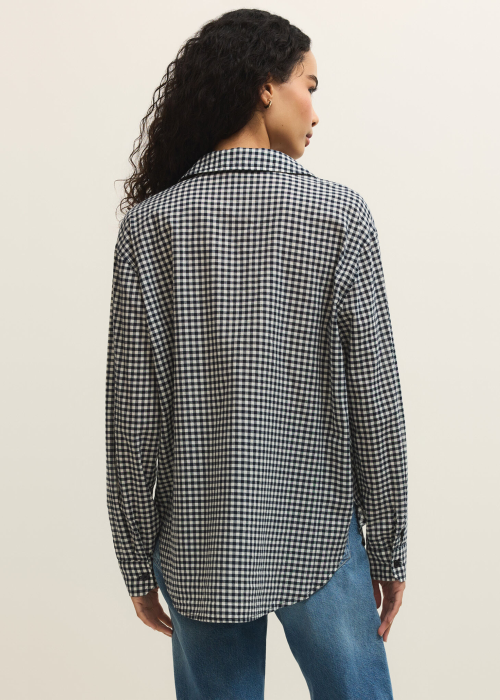 Woman turned around wearing a navy and white gingham button down with jeans