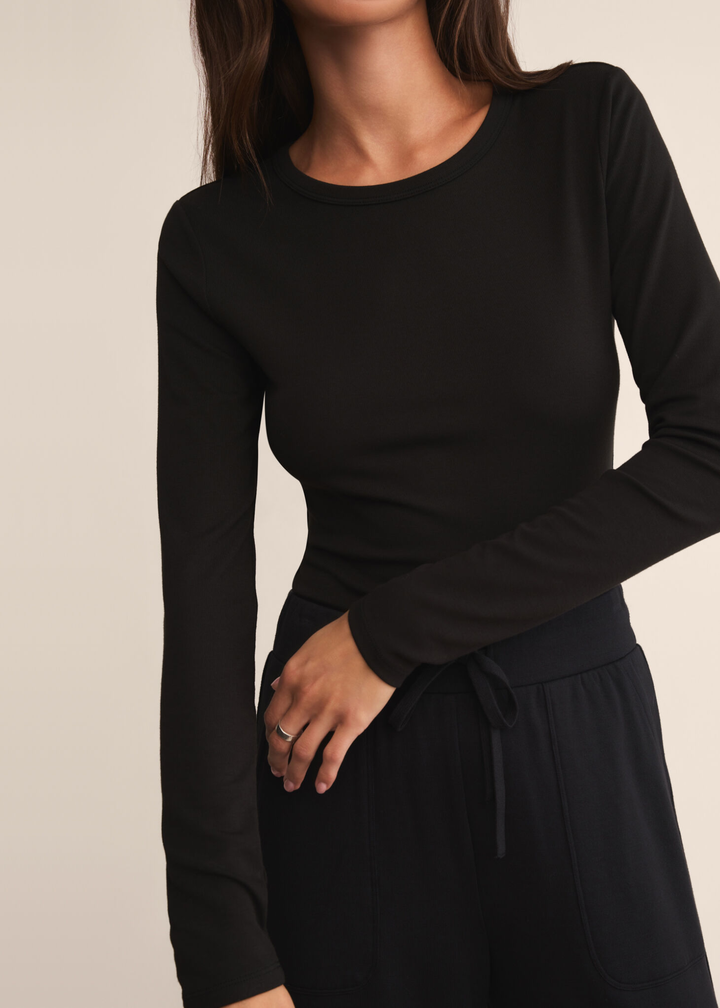Close up of a woman wearing a long sleeve black crew neck shirt with black pants and standing in front of a white background