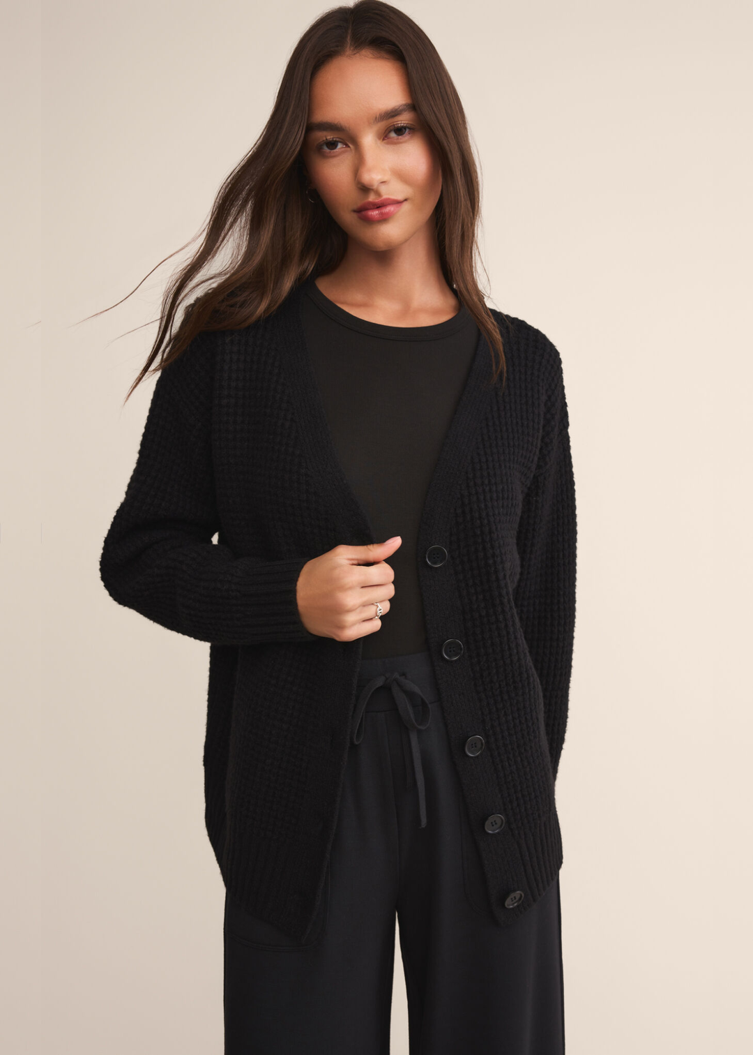 Woman wearing a long sleeve black crew neck shirt with a black cardigan and black pants and standing in front of a white background