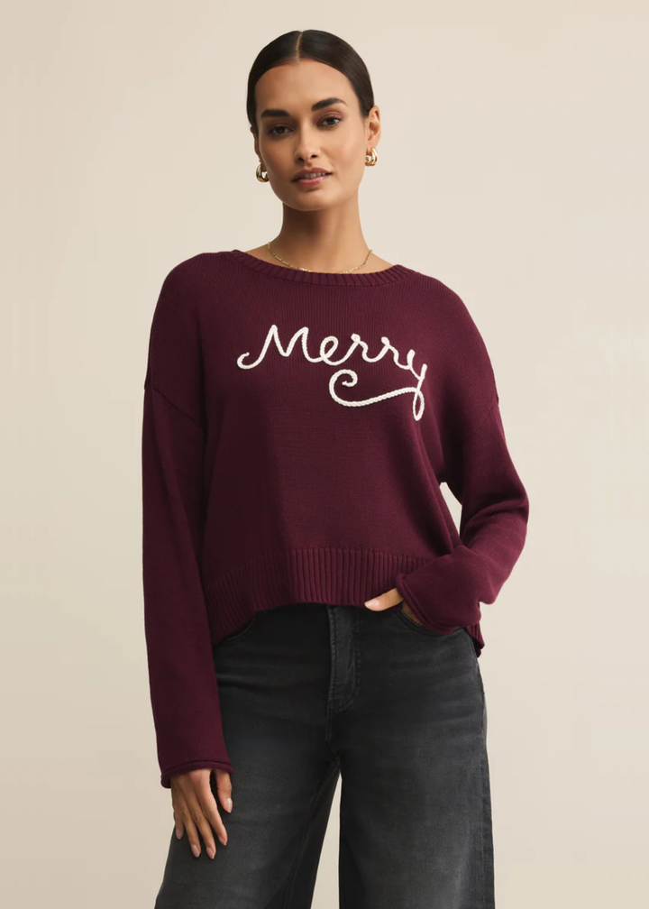 Woman wearing a maroon sweater with white "Merry" lettering in front of a tan background