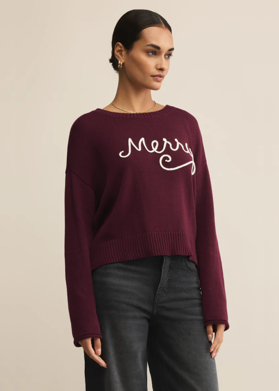 Woman turned to the side wearing a maroon sweater with white "Merry" lettering in front of a tan background