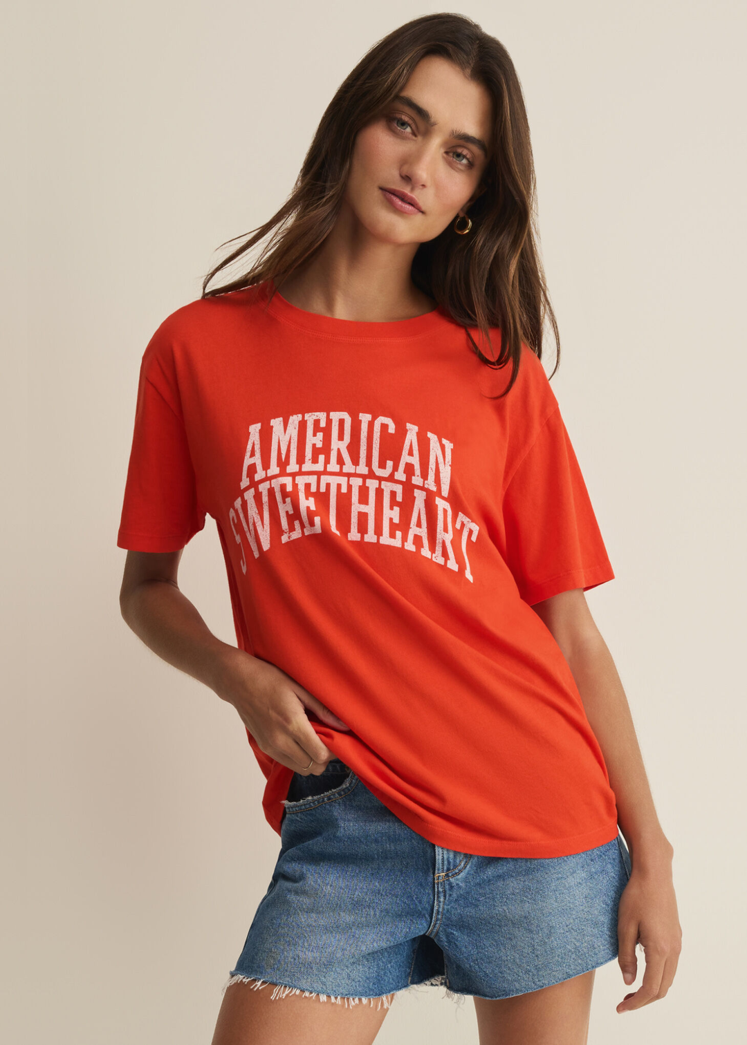 Woman wearing a red t-shirt with an "American Sweetheart" graphic and denim shorts