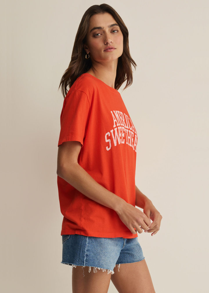Woman wearing a red t-shirt with an "American Sweetheart" graphic and denim shorts