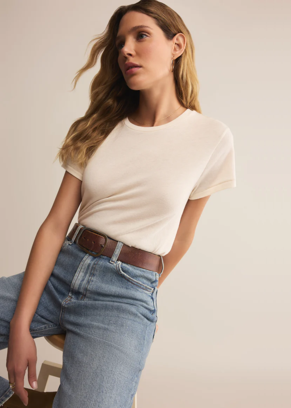 Woman wearing a white short sleeve shirt with jeans sitting in front of a white background