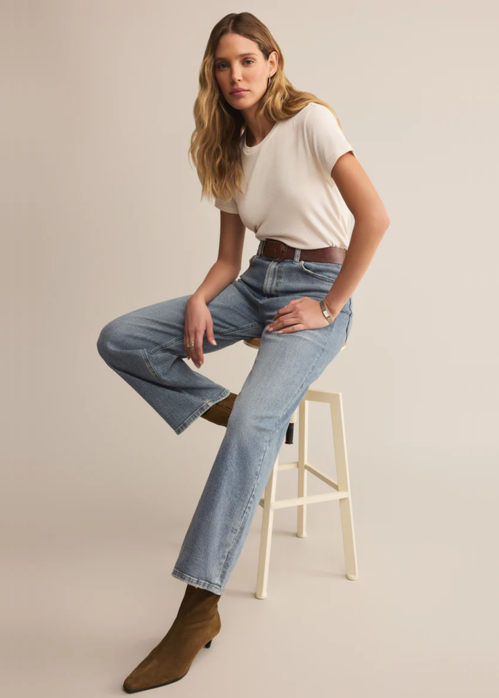 Woman wearing a white short sleeve shirt with jeans and brown boots sitting in front of a white background
