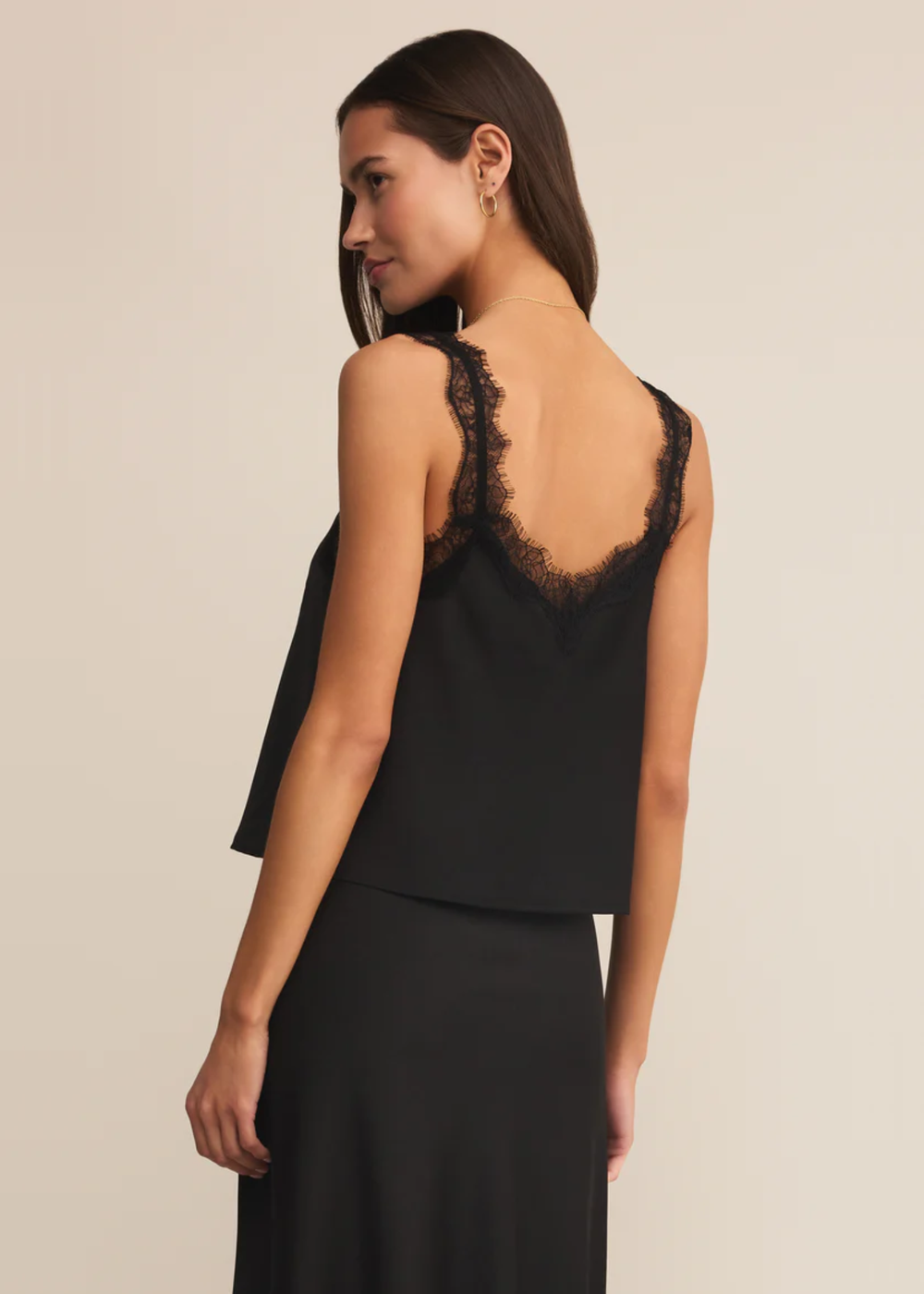 Woman turned to the side wearing a black satin cami with black lace trim with a matching skirt