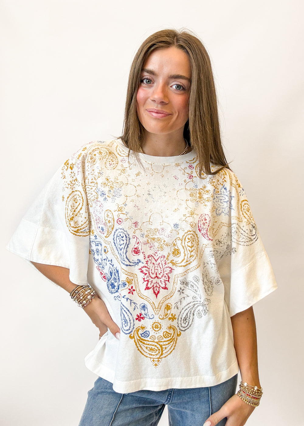 Woman wearing a white t-shirt with colorful paisley patterns on a plain background