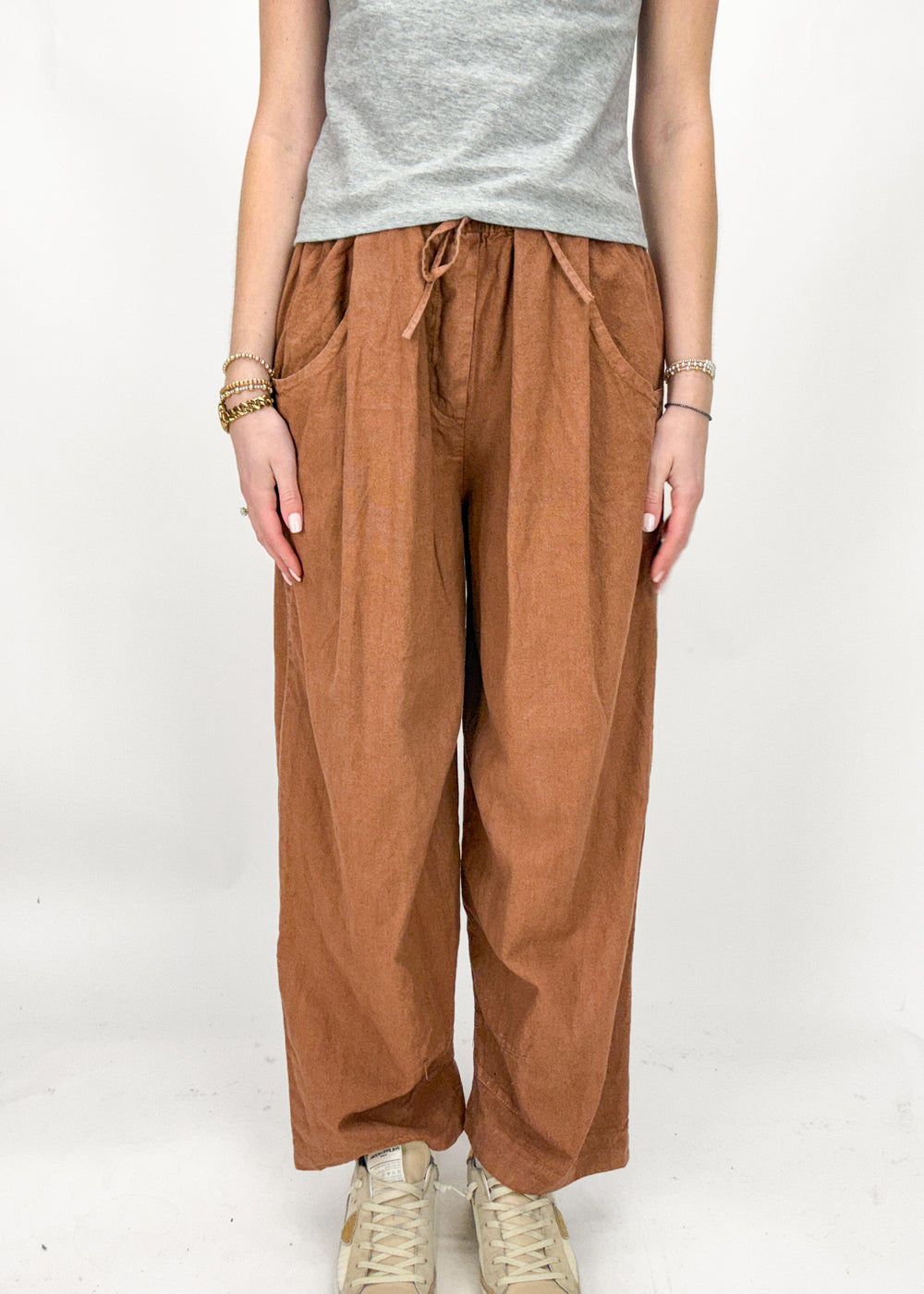 Person wearing rust wide-leg pants and a gray top on a white background