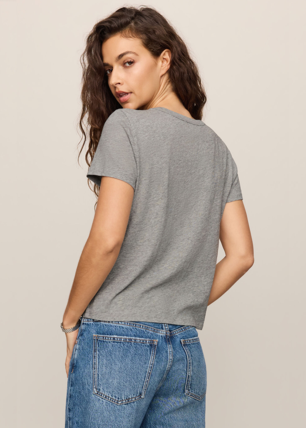 Women wearing grey tee turned around looking over her shoulder. 
