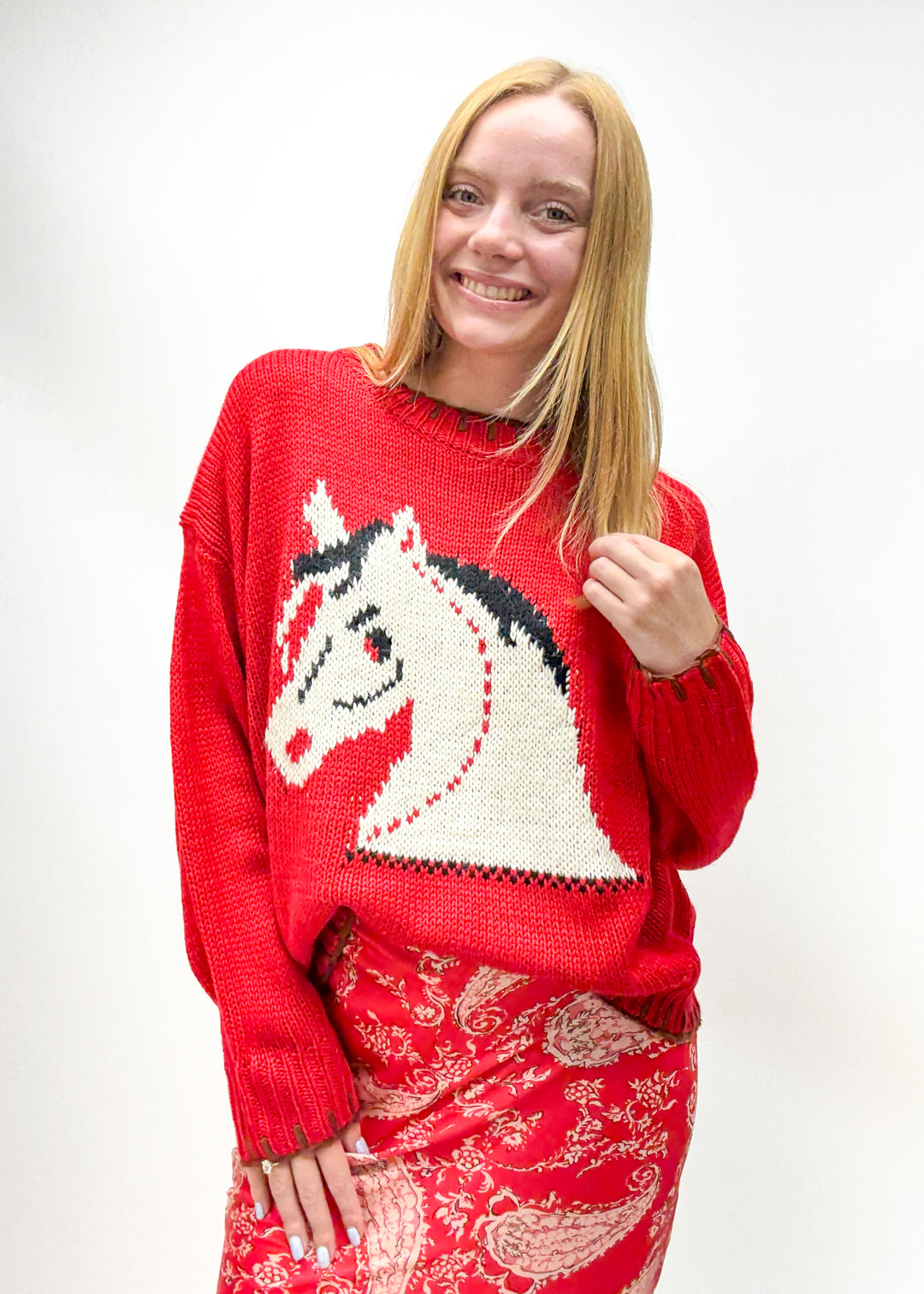 woman wearing red knit sweater with pony chest graphic and brown whipstitch details on sleeves, hem, and collar