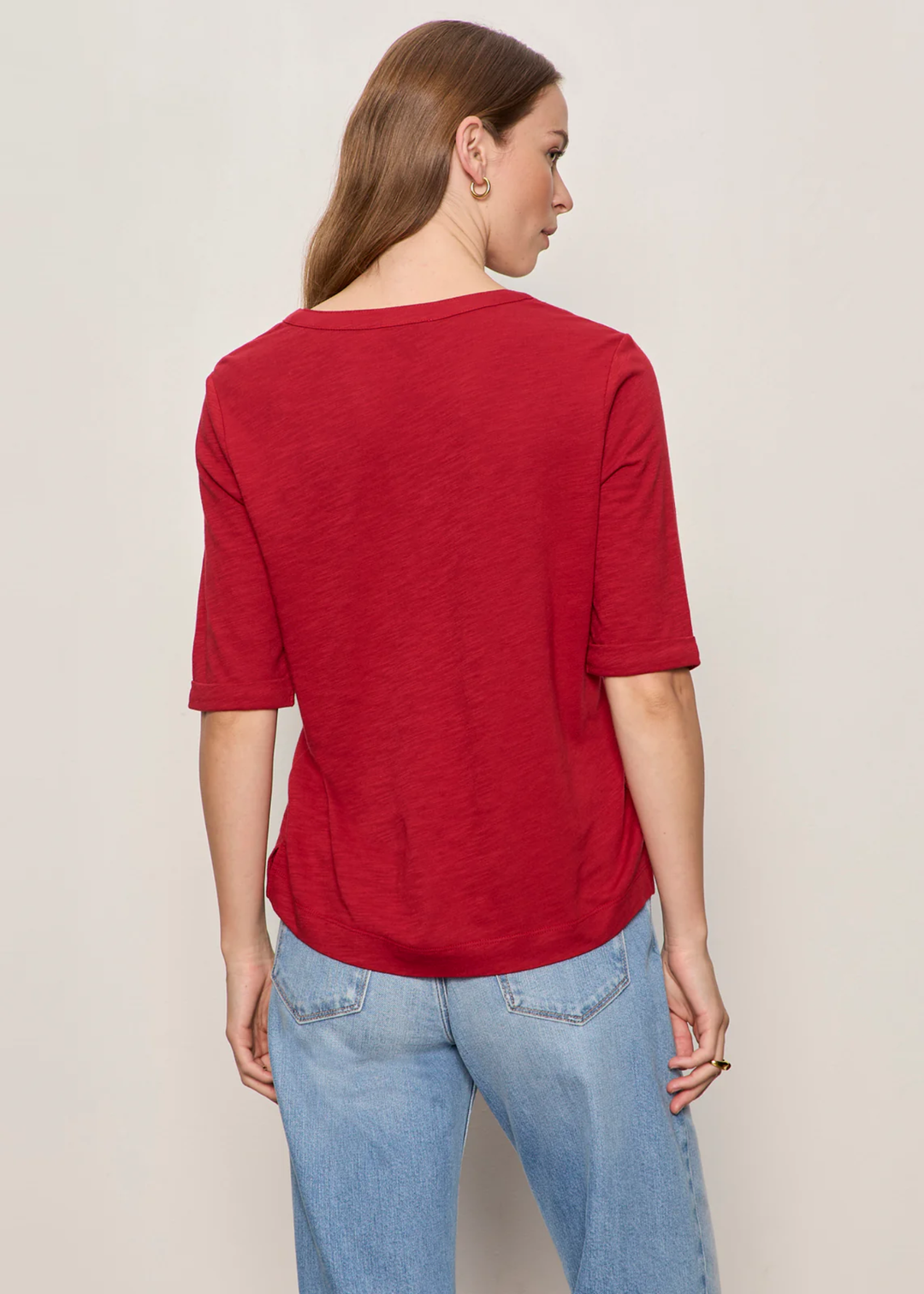 Woman wearing red top with notch neck and turned around. 