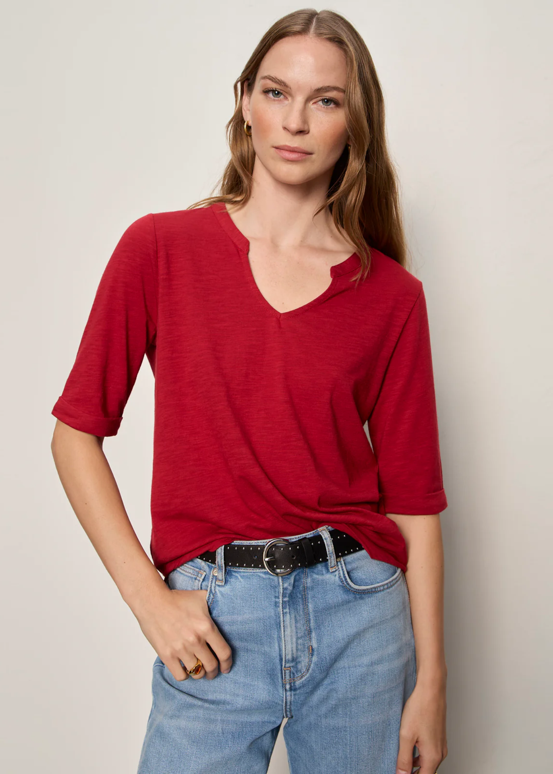 Woman wearing red top with notch neck and hand in her pocket.