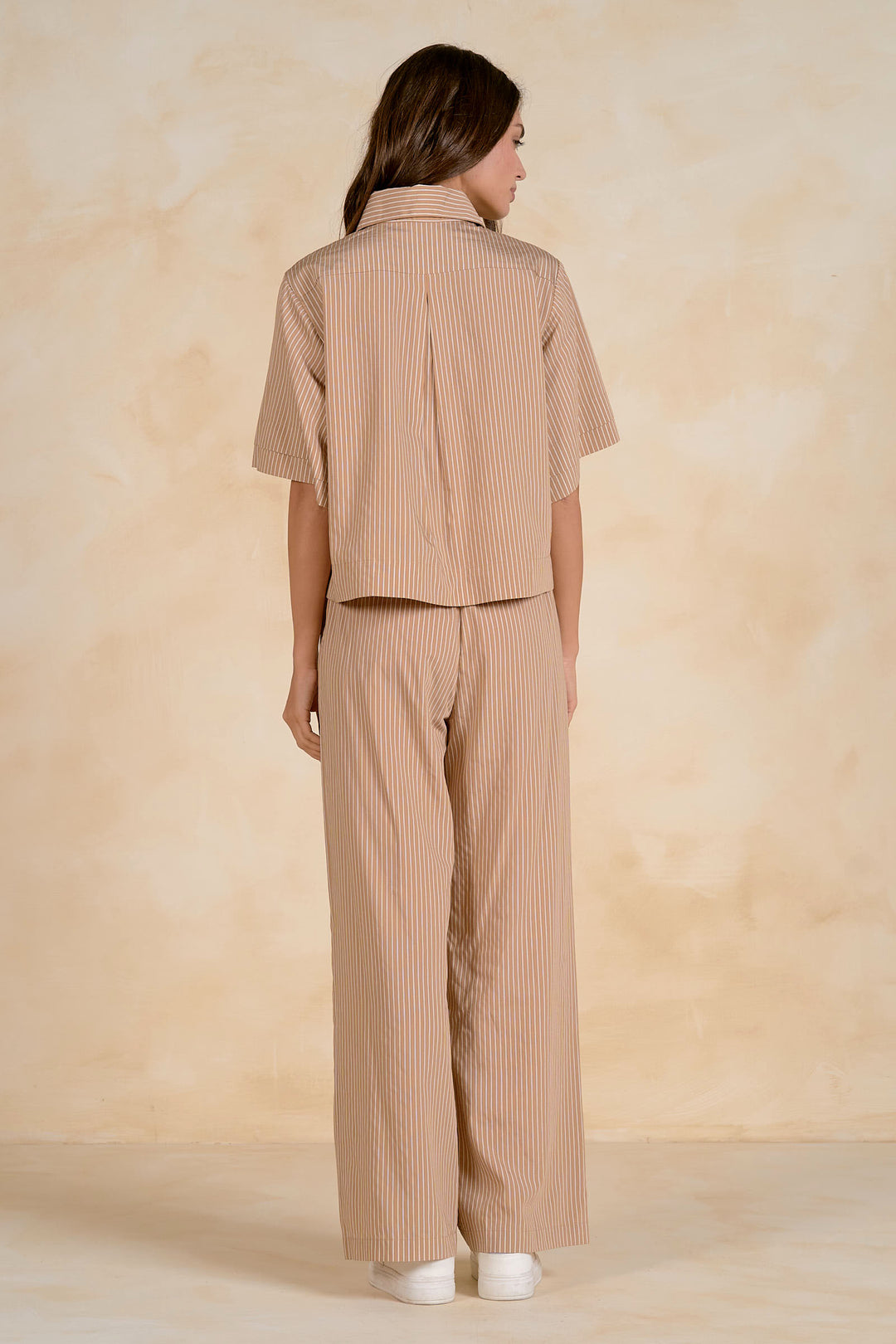 Woman wearing a beige striped shirt and pants against a beige background