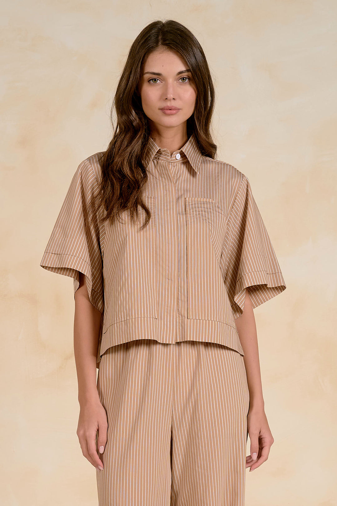 Woman wearing a beige striped shirt and pants against a beige background