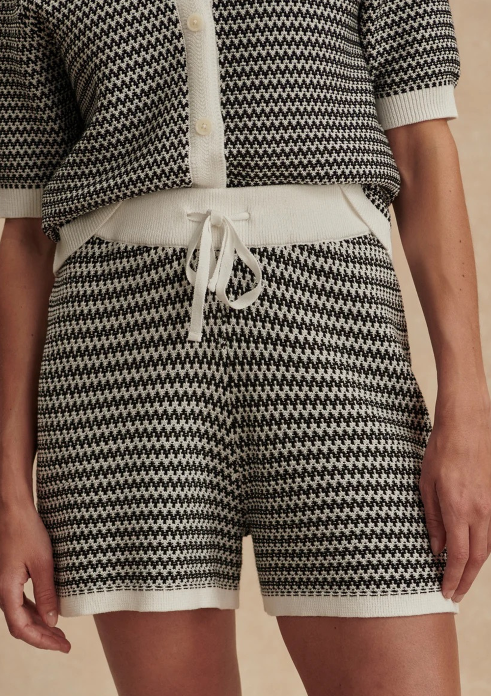 Person wearing a black and white patterned outfit with shorts and a top on a beige background