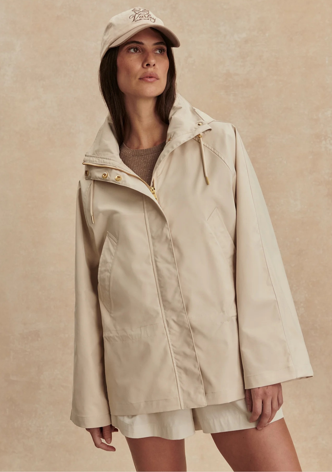 Woman wearing a beige raincoat and cap against a beige background