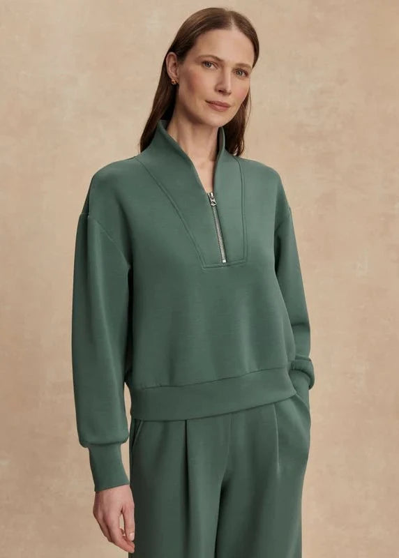 Woman wearing a green zip-up sweatshirt and pants against a beige background