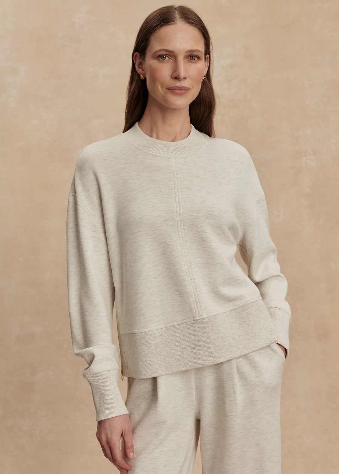 Woman wearing a light gray sweater and pants against a beige background