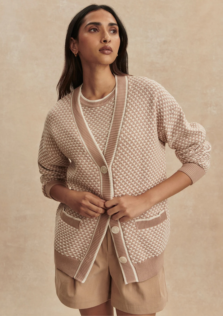 Woman wearing a beige and brown patterned cardigan over a matching top with beige shorts on a beige background.