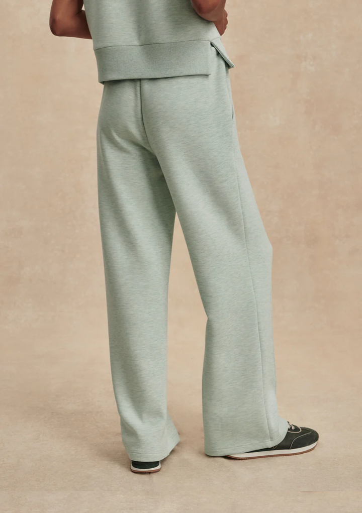 A person shown from the back wearing light sage green wide-leg sweatpants and a matching top, standing against a warm beige studio backdrop.