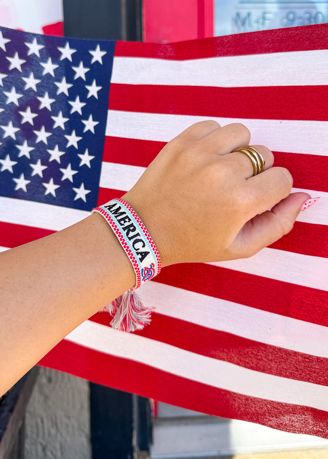 Hand wearing a 'AMERICA 250' bracelet with an American flag in the background