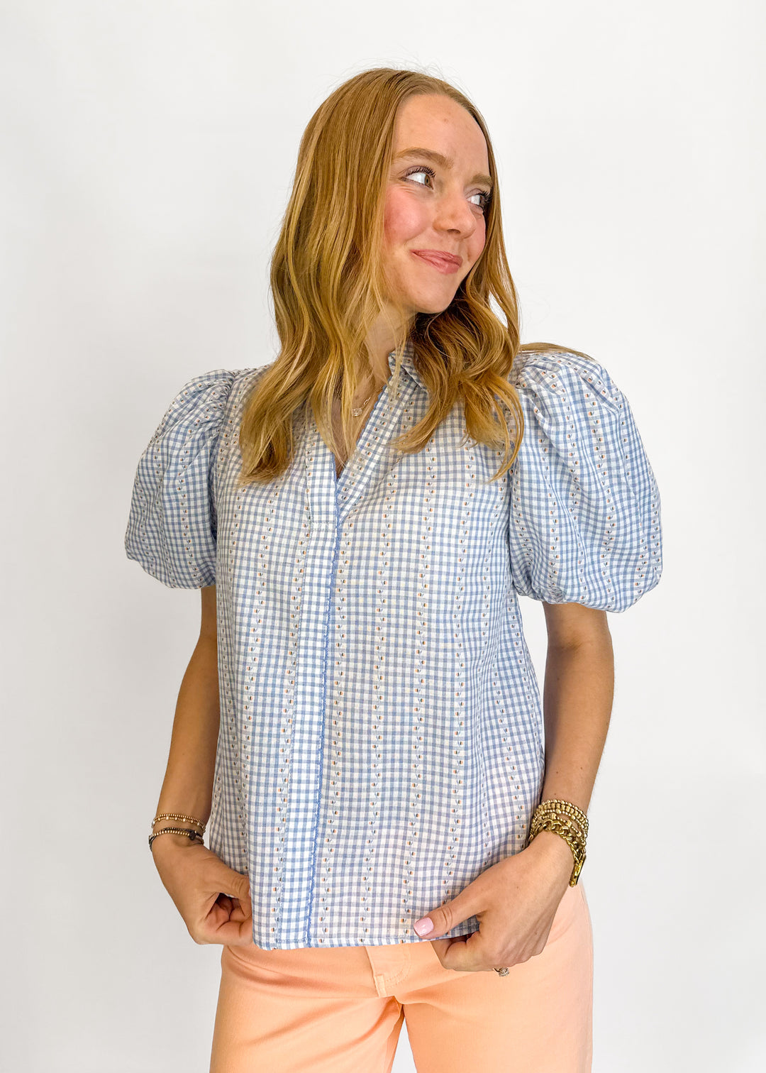Woman wearing a checkered blouse with puff sleeves against a white background