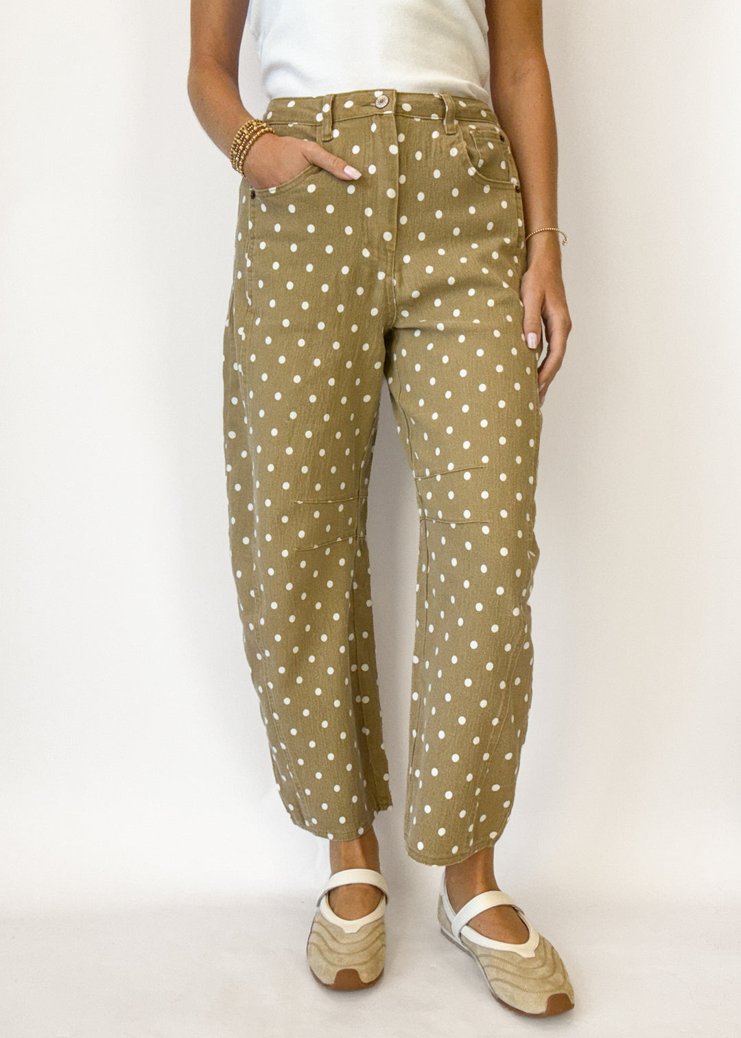 A person wearing beige cropped pants with a white polka dot pattern, styled with a white top and beige Mary Jane shoes against a plain white background.