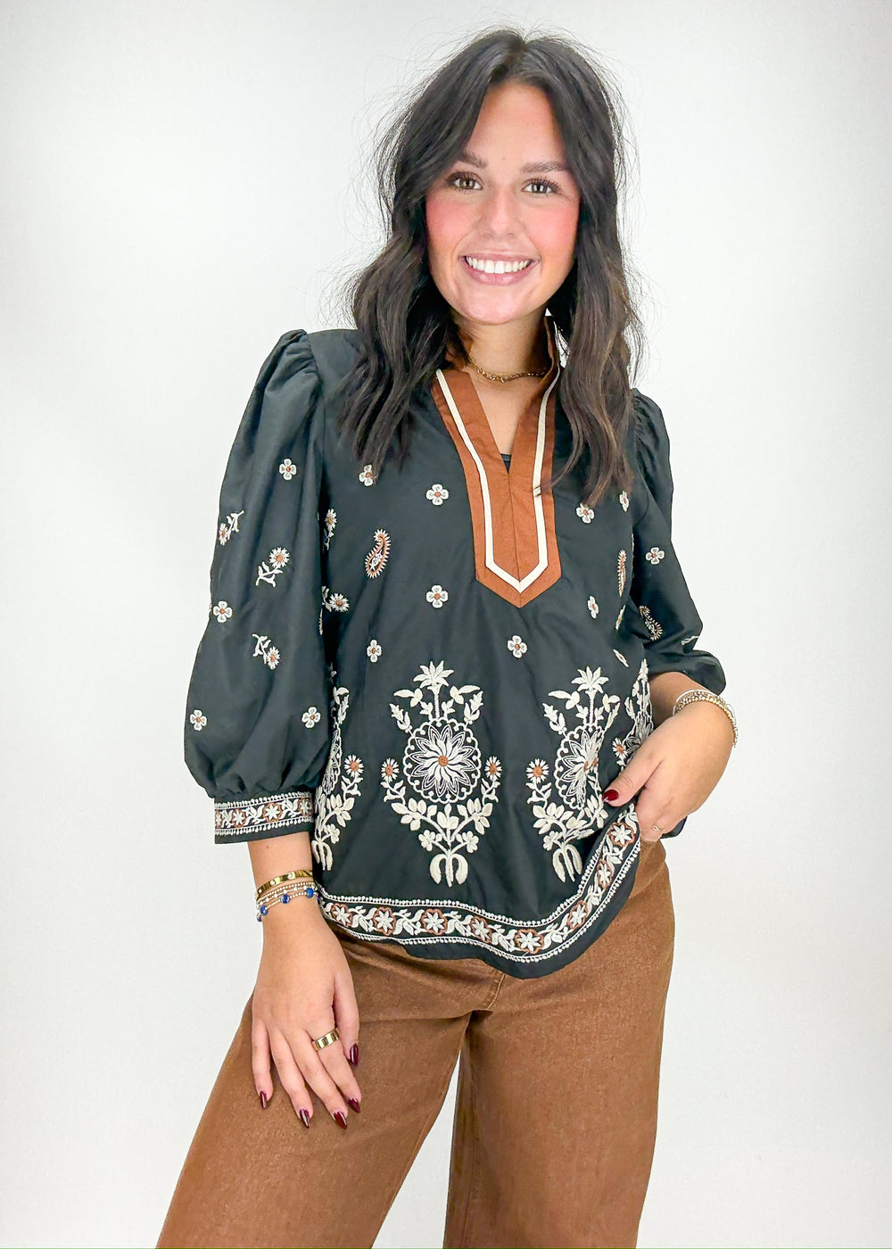 Woman wearing a dark green blouse with intricate patterns 