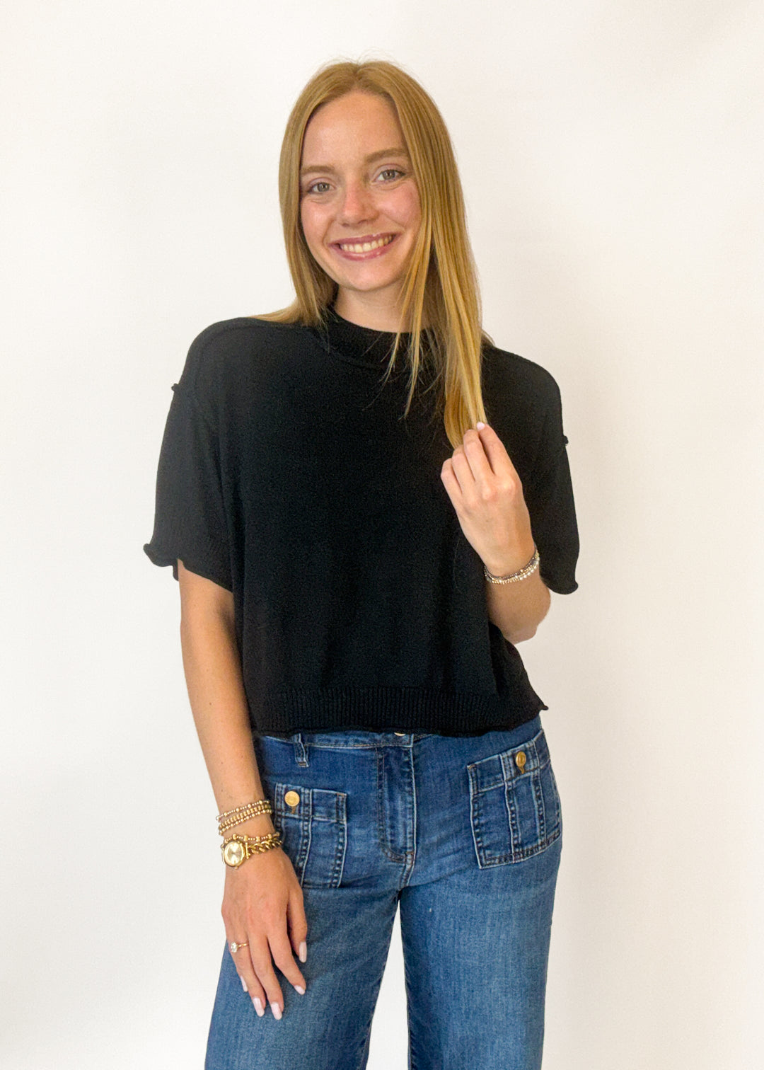Woman wearing a black top and blue jeans against a white background