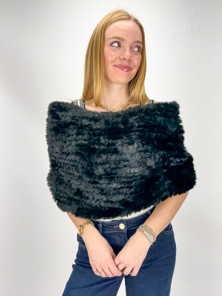Woman wearing a black faux fur shrug over a white top 