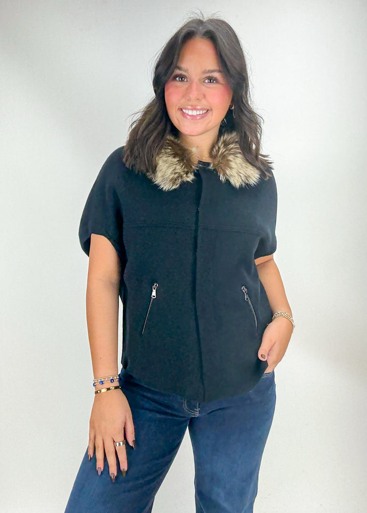 Woman wearing a black vest with fur collar and blue jeans 