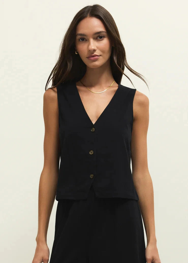 Woman wearing a black sleeveless top with buttons on a plain background