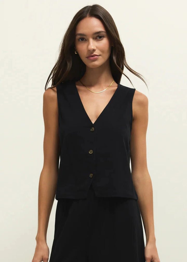 Woman wearing a black sleeveless top with buttons on a plain background