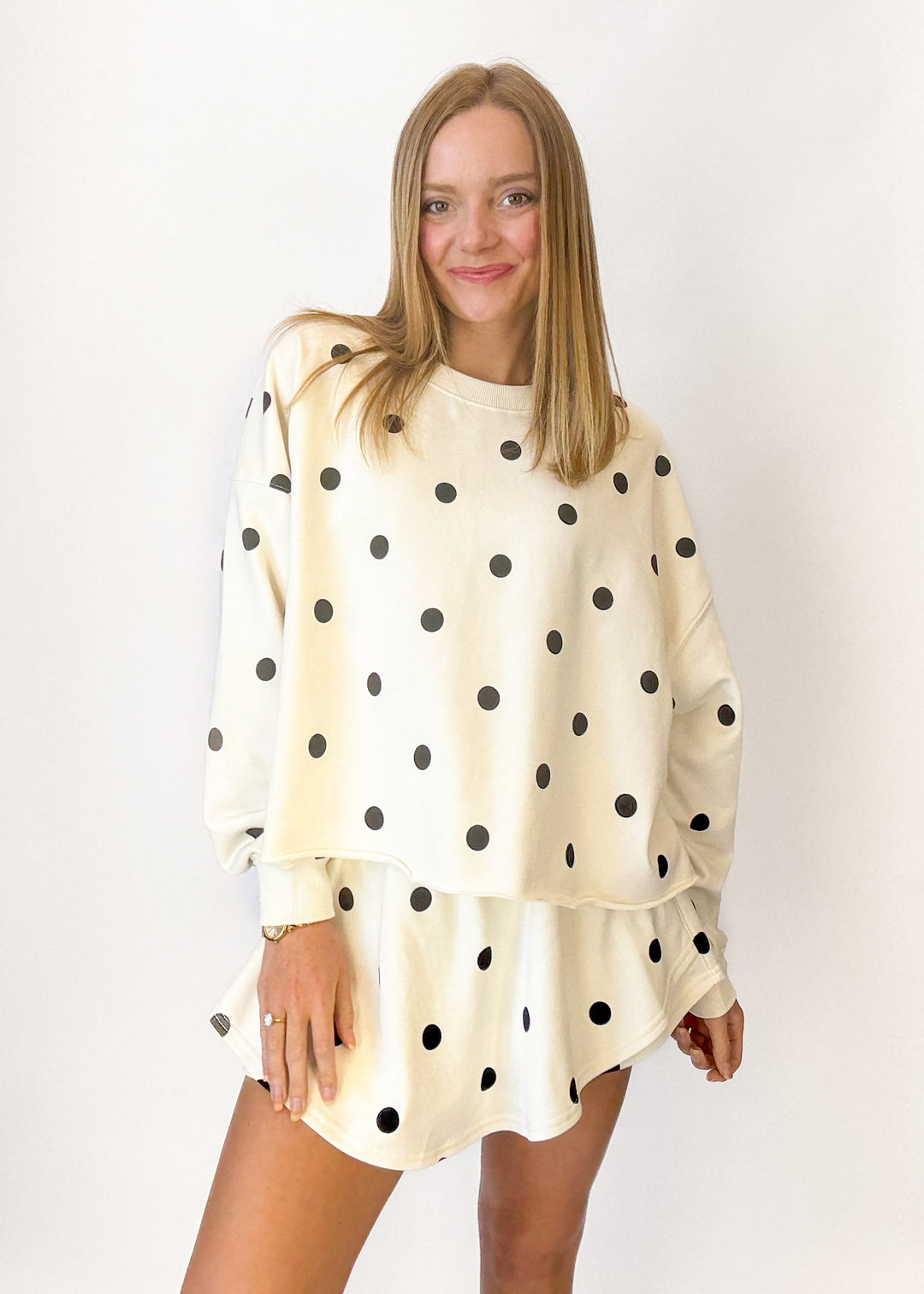 Woman wearing a cream-colored sweatshirt with black polka dots on a white background