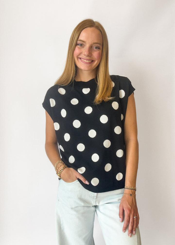 Woman wearing a black top with white polka dots against a plain background