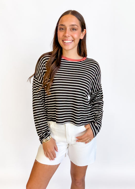Woman wearing a black and white striped long-sleeve top and white shorts on a white background