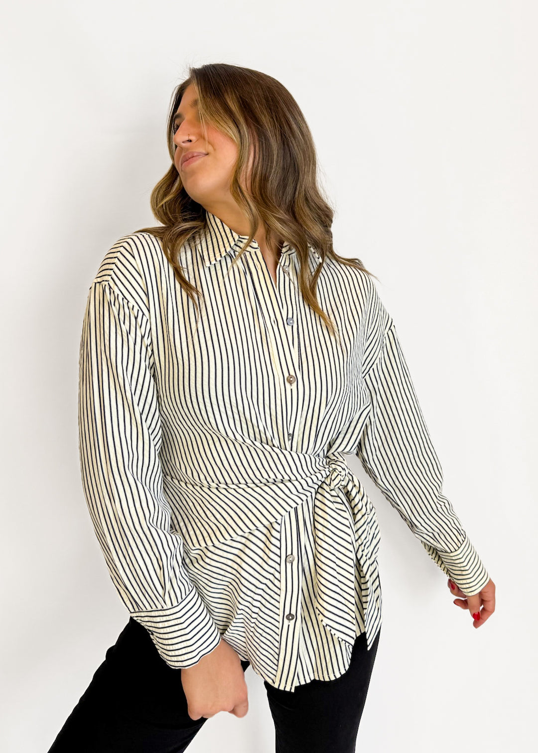 A woman wearing a long-sleeve button-up shirt with vertical black and beige stripes, styled with black pants against a plain white background.