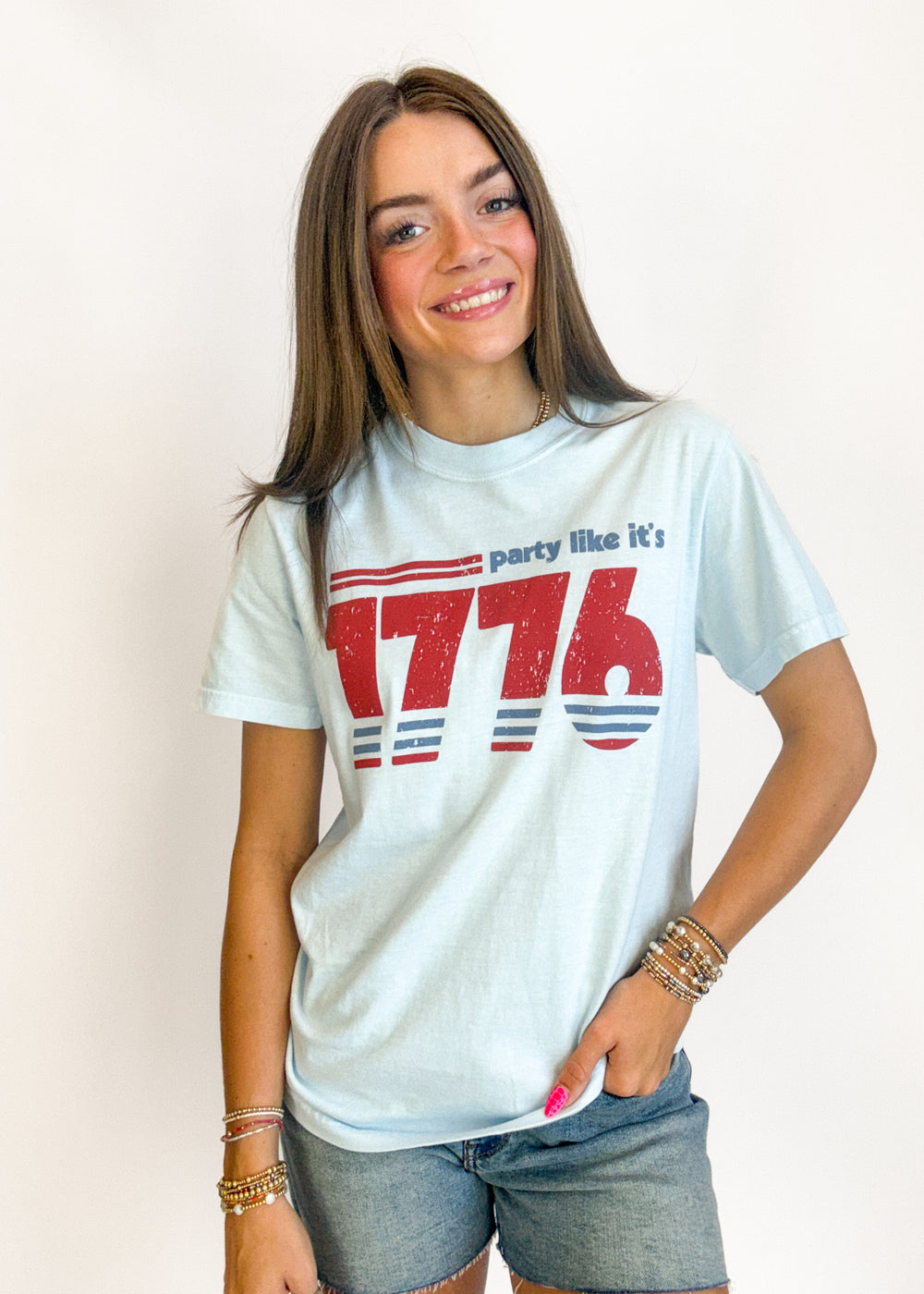 Woman wearing a white t-shirt with 'party like it's 1776' text and red and blue design.