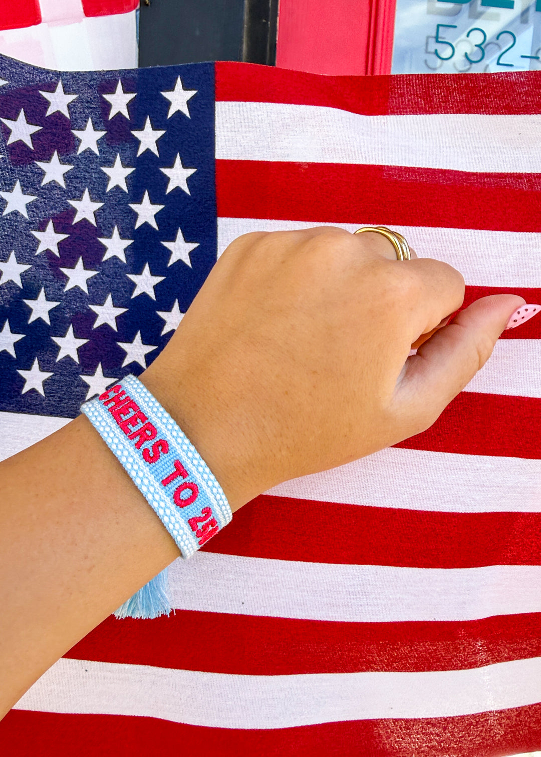 Hand wearing a blue wristband with text, in front of an American flag