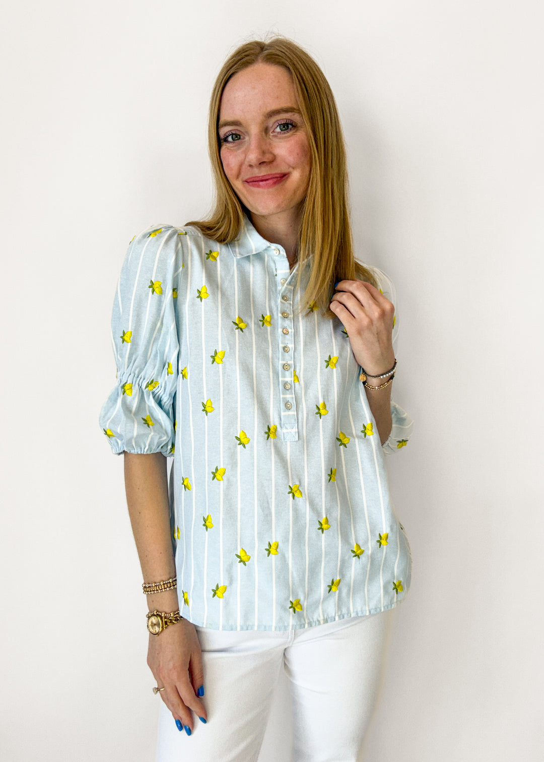 Woman wearing a light blue blouse with yellow floral patterns against a white background