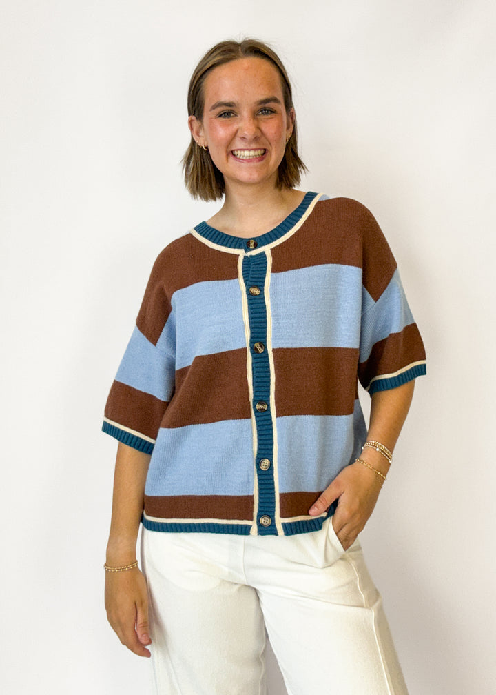 A woman wearing a brown, light blue, and teal striped knit cardigan sweater with cream trim