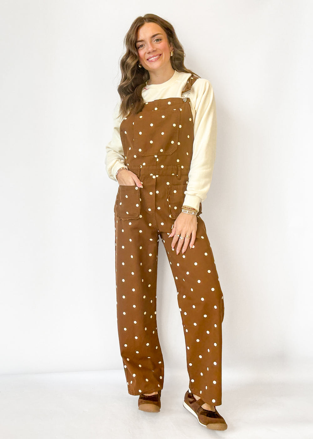 A woman modeling a pair of brown overalls with white polka dots