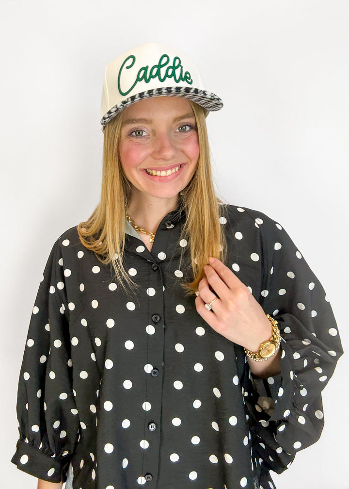 Person wearing a black polka dot shirt and a cap with 'Caddie' text on a white background