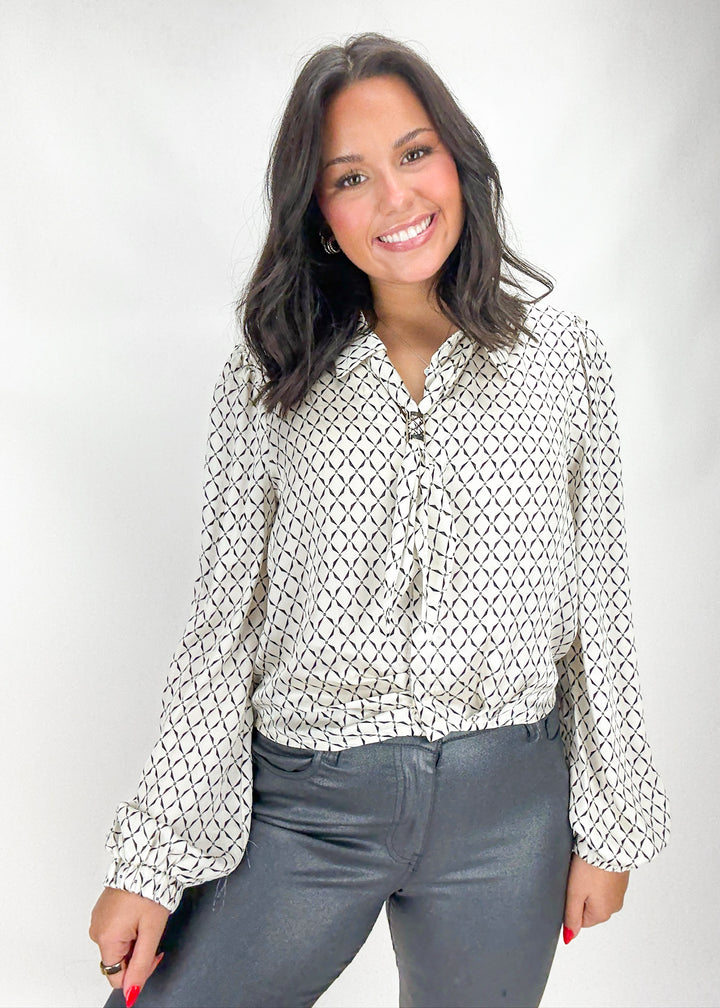 Woman wearing a patterned blouse and gray pants against a white background