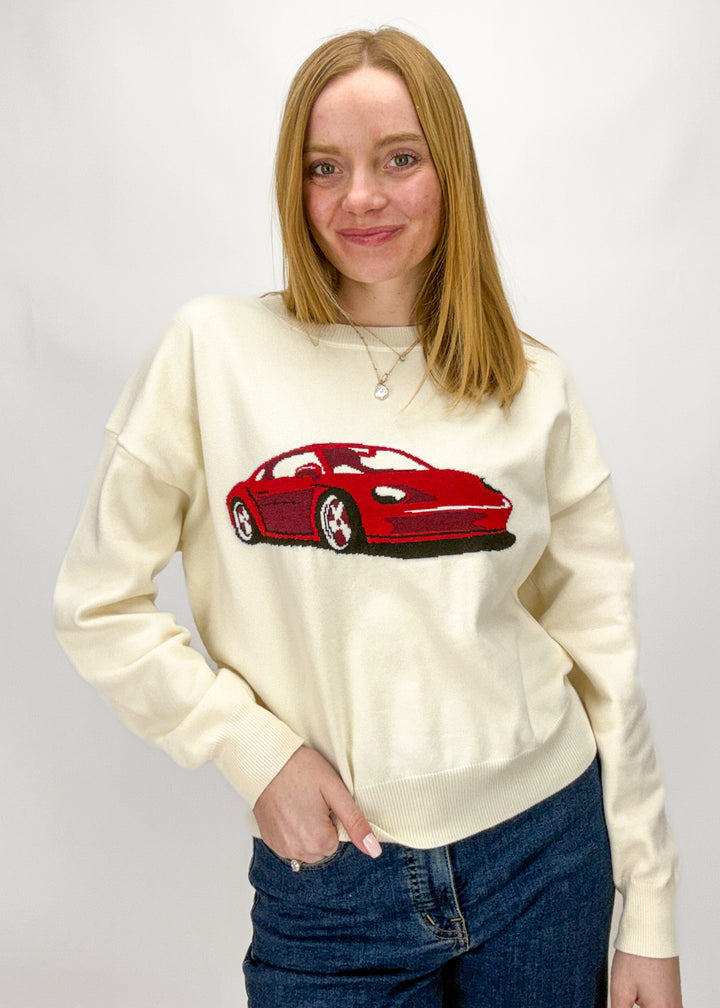 Person wearing a cream sweatshirt with a red car graphic on a plain background