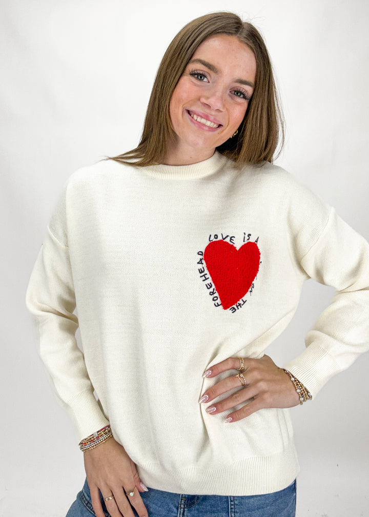 Woman wearing a cream sweater with a red heart design on a white background